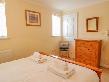 A bedroom with a bed, folded towels, a wooden chair with a cushion, a wooden dresser, a wall mirror and a framed picture at Hops House in Brewers Quay Harbour