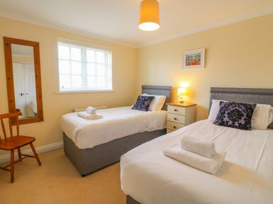 A bedroom with two single beds a wooden chair a wall mirror and a bedside table with a lamp at Hops House in Brewers Quay Harbour