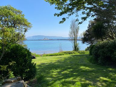 A grassy area with trees and bushes overlooking a body of water with a distant island at Hops House in Brewers Quay Harbour
