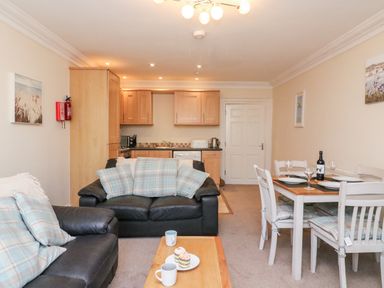 A living room with black sofas and a dining table with chairs next to a kitchen area at Harbour Watch Apartment 1 Brewers Quay Harbour