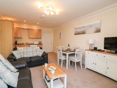 An open plan living and dining area with two black leather sofas and a wooden coffee table with cups and cupcakes at Harbour Watch Apartment 1 Brewers Quay Harbour