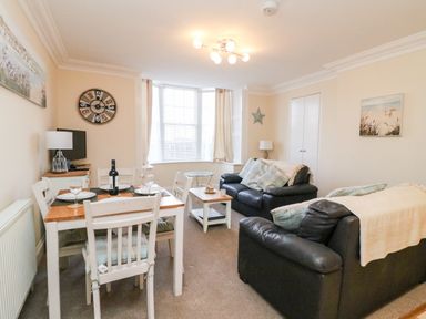 A living room with two black sofas a dining table set with plates and glasses and a wall clock at Harbour Watch Apartment 1 in Brewers Quay Harbour