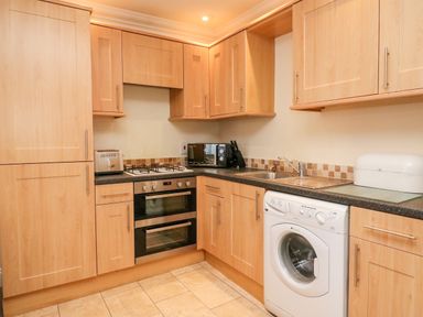 A kitchen with wooden cabinets a washing machine an oven a gas stove a toaster and a microwave at Harbour Watch Apartment 1 Brewers Quay Harbour