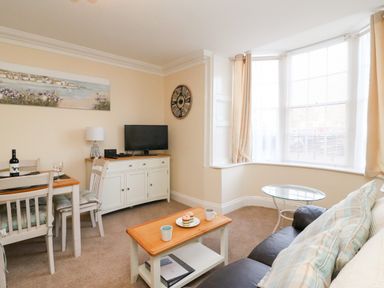 A living room with a dining table chairs a television on a cabinet a coffee table with cups and pastries and a window with curtains at Harbour Watch Apartment 1 Brewers Quay Harbour