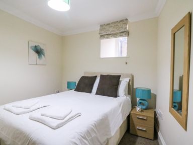 A bedroom with a double bed white bedding two brown pillows bedside tables with blue lamps a window with a patterned blind and a wall mirror at Harbour Watch Apartment 1 Brewers Quay Harbour