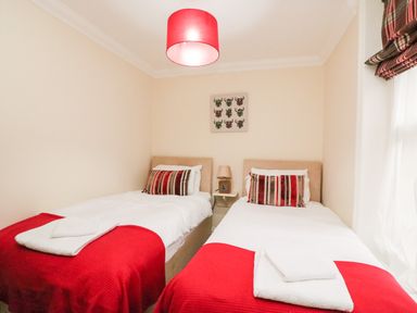 A bedroom with two single beds a small nightstand with a lamp and framed artwork above the beds at Harbour Watch Apartment 1 Brewers Quay Harbour