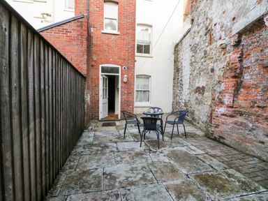An outdoor patio area with stone flooring a round table with three chairs a brick wall a wooden fence and a doorway at Harbour Watch Apartment 1 Brewers Quay Harbour