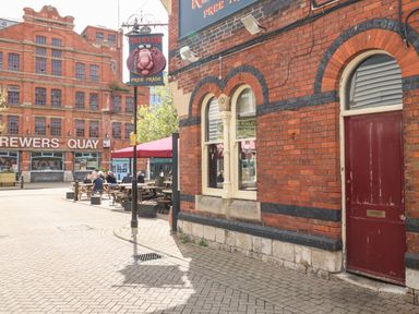 A street scene with a red brick building and a sign reading The Red Lion above outdoor seating at Brewers Quay Harbour
