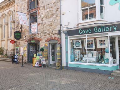 A street view showing Londis Harbour Stores and Cove Gallery with various signs and displayed items on Trinity Street