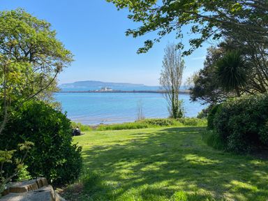A grassy area with trees and bushes overlooking a body of water with an island in the distance at Harbour Watch Apartment 1 Brewers Quay Harbour