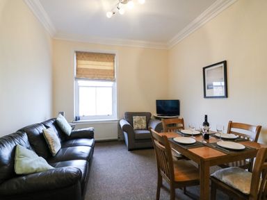 A living room with a black leather sofa, armchair, dining table set with plates and glasses, and a television at Harbour Watch Apartment 6 Brewers Quay Harbour