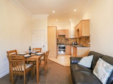 A kitchen and dining area with wooden table and chairs next to a black sofa at Harbour Watch Apartment 6 Brewers Quay Harbour