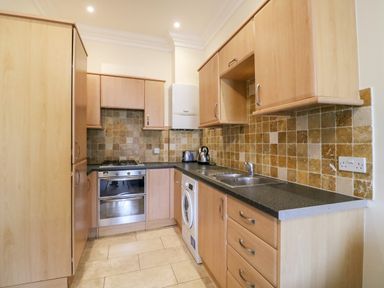 A kitchen with wooden cabinets a gas stove oven washing machine and tiled backsplash at Harbour Watch Apartment 6 Brewers Quay Harbour