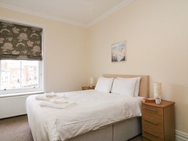 A bedroom with a double bed bedside tables and a window with floral blinds at Harbour Watch Apartment 6 Brewers Quay Harbour