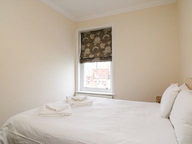 A bedroom with a bed folded towels pillows and a window with a floral blind at Harbour Watch Apartment 6 Brewers Quay Harbour