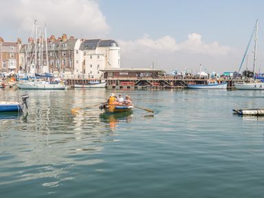A small rowboat with people on a harbor with sailboats and buildings in the background at Brewers Quay Harbour
