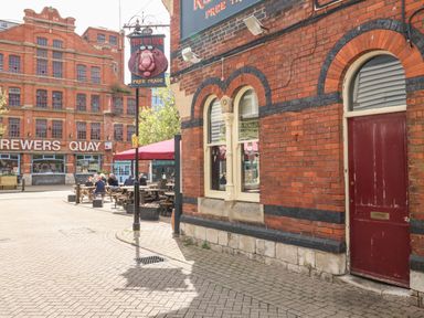 A street view with red brick buildings including The Red Lion pub and Brewers Quay with outdoor seating and people sitting at picnic tables