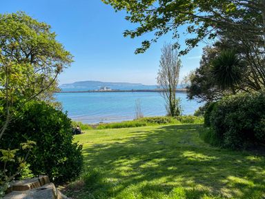 A grassy area with trees by the water and an island visible in the distance at Brewers Quay Harbour
