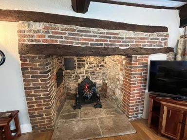 A fireplace with a wooden beam and stone wall at Ivy Cottage in West Lulworth
