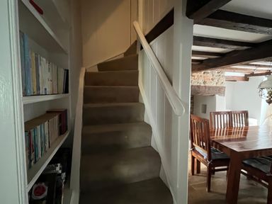 A staircase with a bookshelf and dining area at Ivy Cottage in West Lulworth