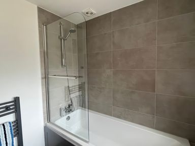 A bathtub with a shower enclosure at Ivy Cottage in West Lulworth