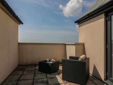 An outdoor patio with a black wicker armchair with cushion and a matching table with a cup and pastry at Jurassic Coast House in Portland