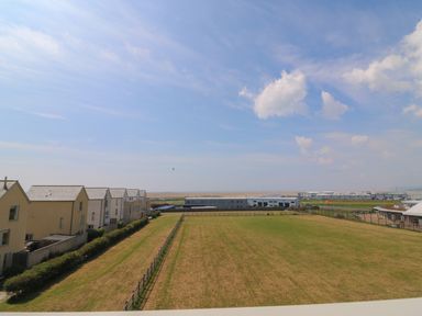 A large fenced grassy field with rows of houses on the left and industrial buildings in the distance at Jurassic Coast House in Portland