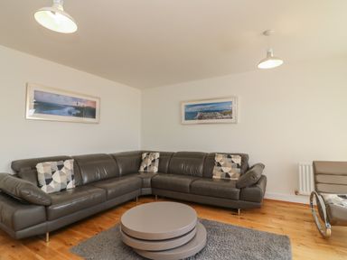 A living room with a gray sectional sofa and patterned pillows a round coffee table and framed pictures on walls at Jurassic Coast House in Portland