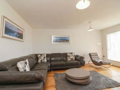 A living room with a sectional leather sofa chairs round coffee table and framed pictures on the wall at Jurassic Coast House in Portland
