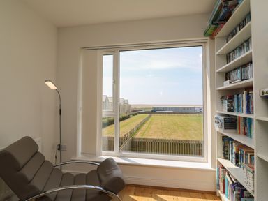 A room with a reclining chair a floor lamp a bookshelf and a large window overlooking a fenced lawn Jurassic Coast House Portland