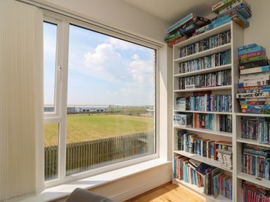 A room with a large window overlooking a grassy field and shelves filled with books and board games at Jurassic Coast House in Portland