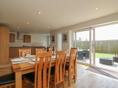 A dining area with a wooden table set with plates and glasses next to a kitchen and sliding glass doors leading to a fenced garden at Jurassic Coast House in Portland