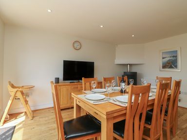 A dining room with a wooden dining table set with plates and glasses and a television on a wooden cabinet at Jurassic Coast House in Portland
