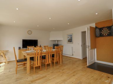 A dining room with a wooden table and chairs a television a clock a dartboard and a door at Jurassic Coast House in Portland