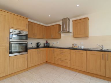 A kitchen with wooden cabinets, a double oven, kettle, toaster, sink, and countertop at Jurassic Coast House in Portland