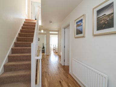 A hallway with wooden floor leading to two rooms and a carpeted staircase on the left at Jurassic Coast House in Portland