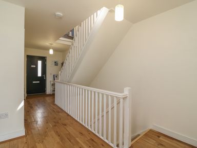 A hallway with wooden floor lighting and a staircase with white railings at Jurassic Coast House in Portland