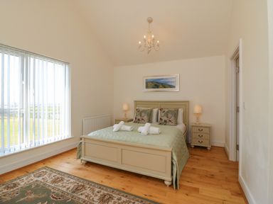A bedroom with a double bed, bedside tables with lamps, a framed picture, a rug, and vertical blinds at Jurassic Coast House in Portland