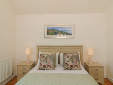 A bedroom with a bed with decorative cushions two bedside tables with lamps and a landscape picture above the bed at Jurassic Coast House in Portland