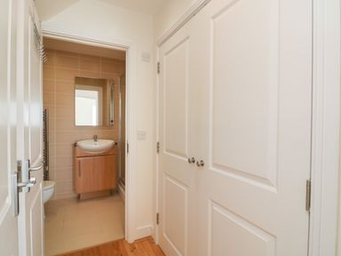 A hallway with white doors and a bathroom with a sink and mirror at Jurassic Coast House in Portland