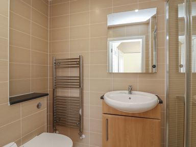 A bathroom with a sink and mirror above a wooden cabinet a toilet a wall-mounted towel radiator and tiled walls at Jurassic Coast House in Portland