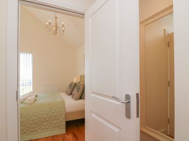 A bedroom with a partially open door a bed with pillows and folded towels a chandelier and a window with vertical blinds at Jurassic Coast House in Portland