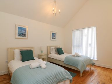 A bedroom with two single beds green pillows light blue covers a nightstand and window blinds at Jurassic Coast House in Portland