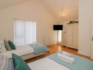 A bedroom with two single beds pillows folded towels wardrobe dresser and a wall-mounted TV at Jurassic Coast House in Portland