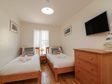 A bedroom with two single beds a wooden dresser a television and a window with blinds at Jurassic Coast House in Portland