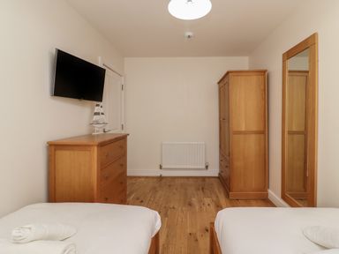 A bedroom with two single beds a wooden dresser a wardrobe a wall-mounted television and a large mirror at Jurassic Coast House Portland