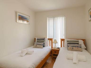 A bedroom with two single beds with white bedding and pillows with a wooden nightstand and lamp between the beds at Jurassic Coast House in Portland