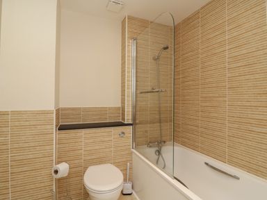 A bathroom with a toilet a toilet brush a bathtub with a showerhead and a glass shower screen at Jurassic Coast House in Portland