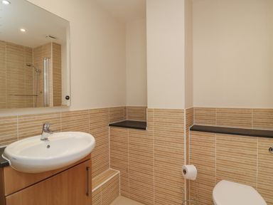 A bathroom with a sink, mirror, toilet, and tiled walls at Jurassic Coast House in Portland