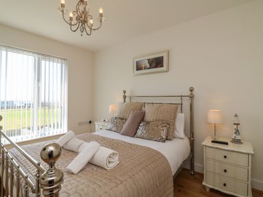 A bedroom with a metal bed frame beige bedding bedside tables with lamps and a window with vertical blinds at Jurassic Coast House in Portland